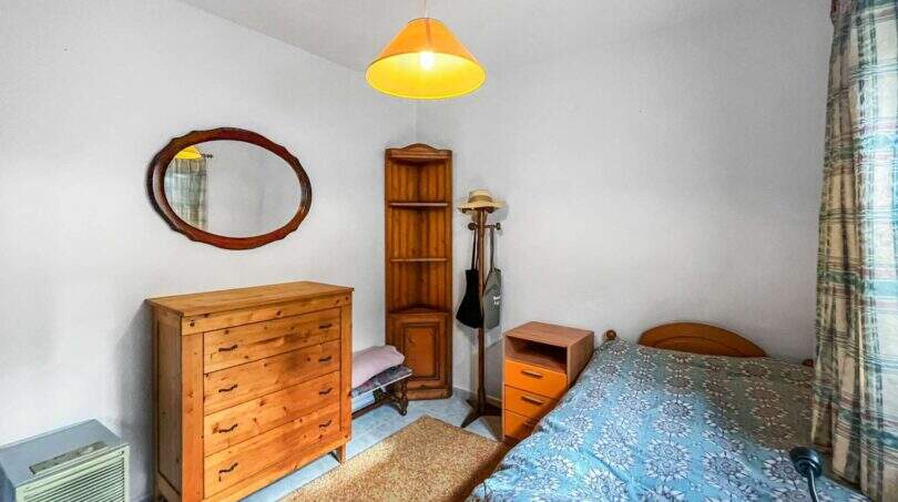 Bedroom with a wooden dresser, mirror, corner shelf, and double bed with a blue bedspread in a house in Felanitx.