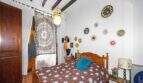 A cozy bedroom with a wooden bed, a mandala tapestry, sun-themed decor, and rustic wooden beams in a house in Felanitx.