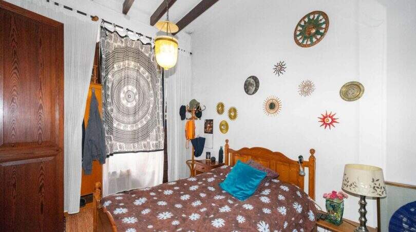 A cozy bedroom with a wooden bed, a mandala tapestry, sun-themed decor, and rustic wooden beams in a house in Felanitx.
