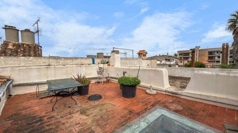Rooftop terrace with terracotta tiles, plants, and a glass roof panel, overlooking neighboring buildings in Felanitx