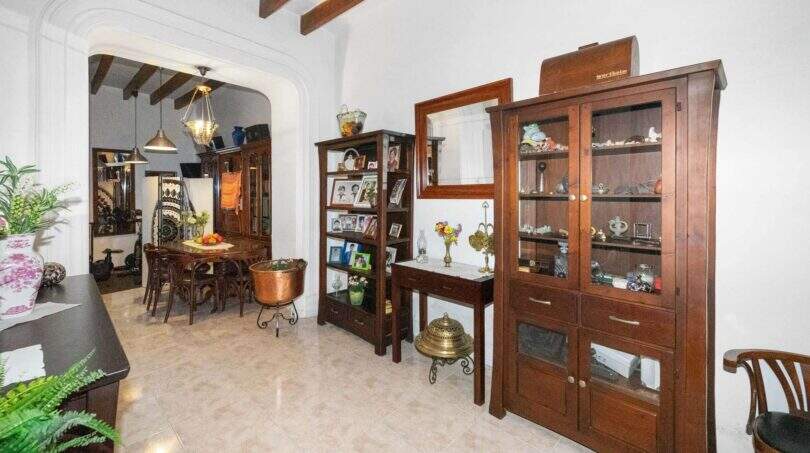 Living room with exposed wooden beams, wooden display cabinets, and a passageway to the dining room in a charming house in Felanitx
