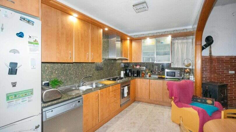 Kitchen with wood cabinet fronts, granite countertops, and built-in appliances, and an adjoining living area with a wood-burning stove in Felanitx