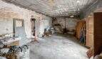 Unrenovated basement room with concrete floor and ceiling; storage area containing various items; in need of renovation