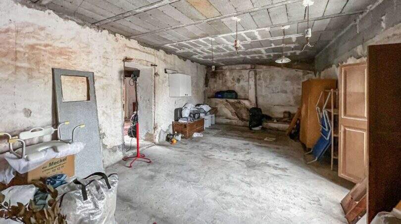 Unrenovated basement room with concrete floor and ceiling; storage area containing various items; in need of renovation