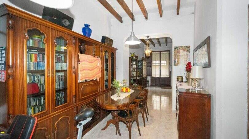 Dining room with a wooden beam ceiling, an antique bookcase, and a round dining table in a house in Felanitx