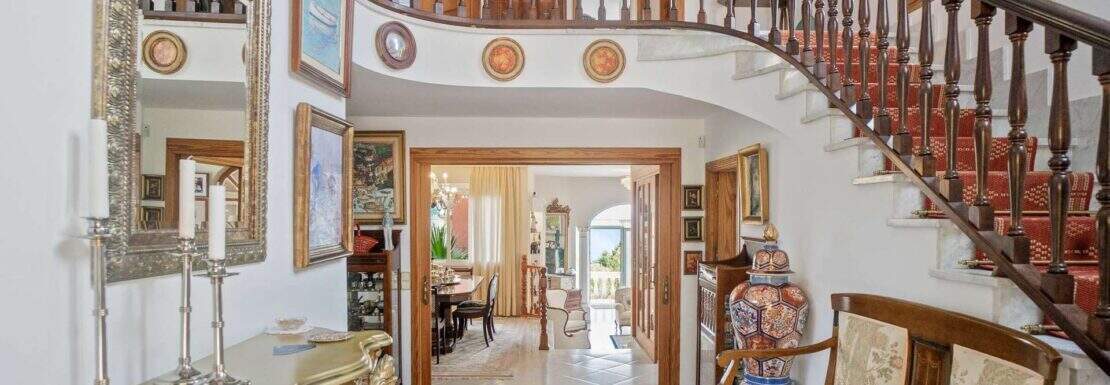 Elegante Eingangshalle mit geschwungener Holztreppe, Kunstwerken und antikem Mobiliar in Villa Costa d'en Blanes