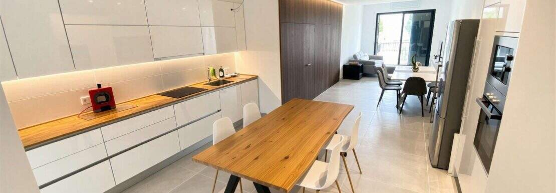 Moderne offene Küche mit Holztisch, weißen Schränken und Blick ins Wohnzimmer der Luxus-Maisonette Porto Cristo