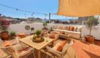 Terraza soleada con zona lounge, mesa de comedor, vistas al mar y plantación mediterránea en Porto Cristo