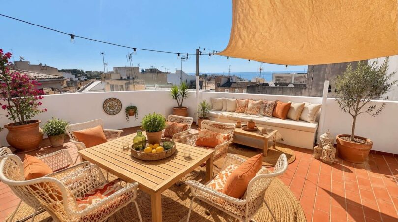 Terraza soleada con zona lounge, mesa de comedor, vistas al mar y plantación mediterránea en Porto Cristo