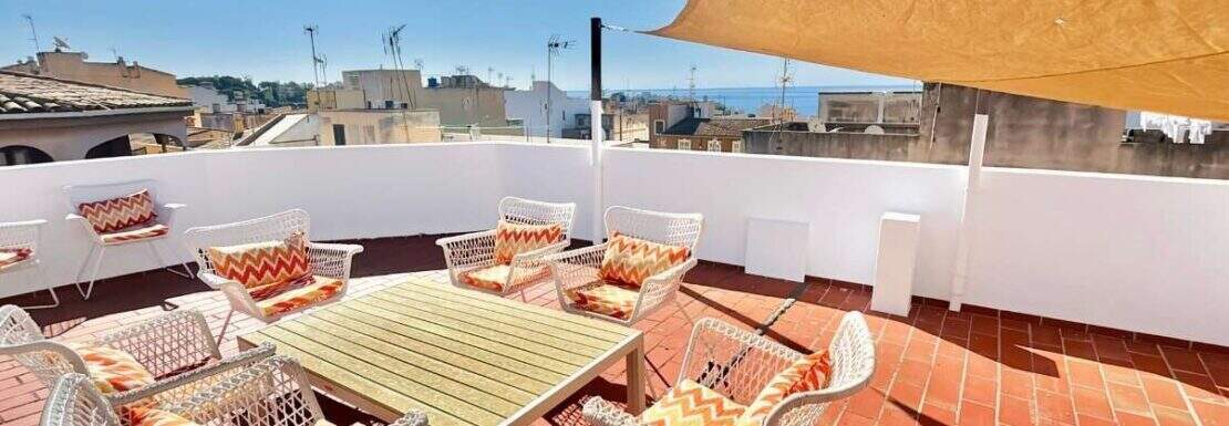 Sonnige Dachterrasse mit Meerblick, weißen Rattanstühlen, Esstisch und Sonnensegel in Porto Cristo
