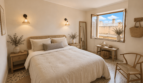 Helles Schlafzimmer mit Rattanbett, Terrazzoböden und geöffnetem Fenster mit Blick auf Porto Cristo