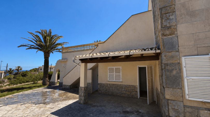 Outdoor area of a Majorcan villa in Manacor with covered entrance, natural stone cladding and palm tree.