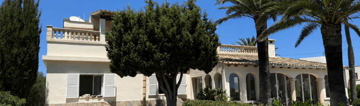 Exterior view of a Mediterranean villa in Manacor with palms, arcades, balustrade and well-maintained garden under blue sky.