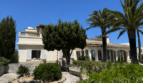 Exterior view of a Mediterranean villa in Manacor with palms, arcades, balustrade and well-maintained garden under blue sky.