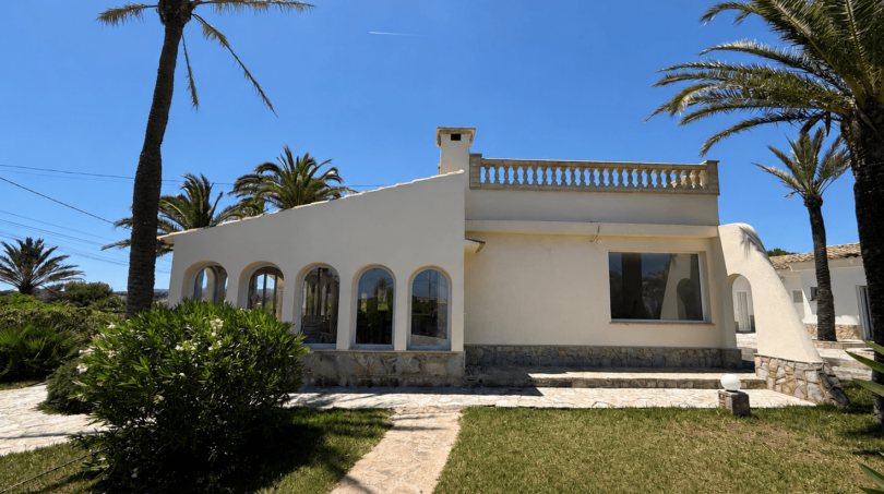 Exterior view of a white Majorcan villa in Manacor with arched windows, balustrade and palms under blue sky.
