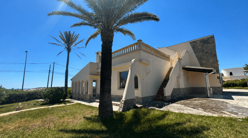 Exterior view of a Majorcan villa in Manacor with palm trees, balustrade, outdoor staircase and Mediterranean garden in brilliant sunshine.