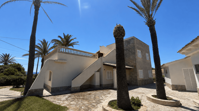 Exterior view of a Majorcan villa in Manacor with palms, stone paving, white façade and external staircase to the roof terrace.