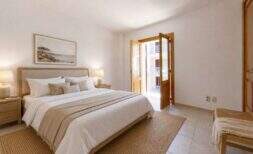 Luminoso dormitorio del dúplex en Porto Cristo con cama de matrimonio, muebles de madera y acceso al balcón con vistas al mar.