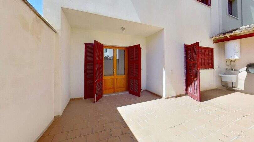 Sonniger Innenhof mit roten Fensterläden und Terrakottaboden der Maisonette in Porto Cristo
