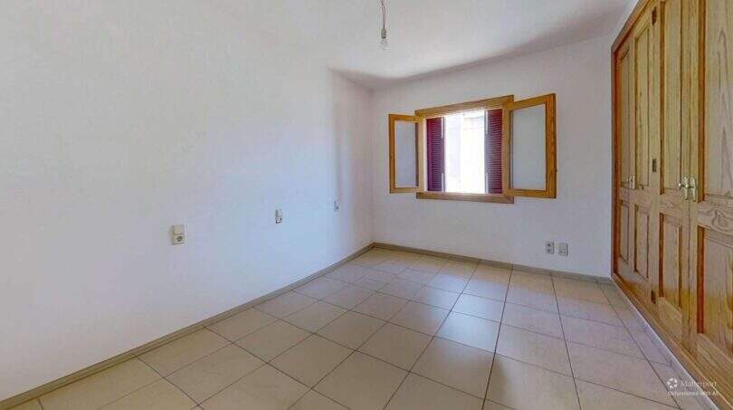 Leeres Schlafzimmer mit Holzkleiderschrank, geöffnetem Fenster mit Holzrahmen und hellem Fliesenboden in Maisonette Porto Cristo