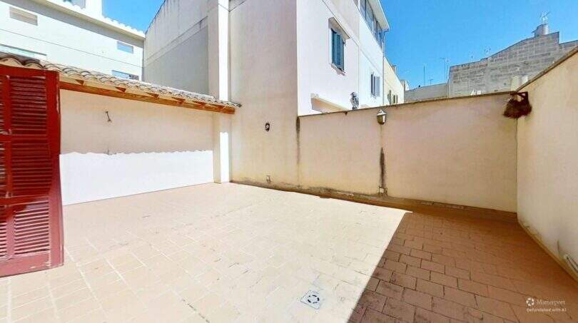 Sonniger Innenhof mit Terrakottafliesen, Wandleuchten und roter Holztür in Maisonette Porto Cristo