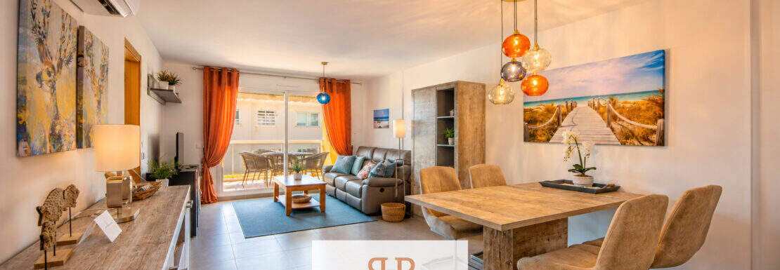 Bright living-dining area in a Mallorca apartment with a wooden table, leather sofa, pendant lights, and access to the terrace.