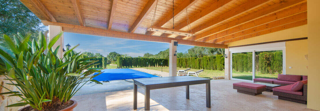 Überdachte Terrasse der Finca Llucmajor mit Holzdecke, Lounge, Esstisch und Pool im Hintergrund.