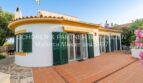 Außenansicht Chalet Cala Murada: weiße Fassade, grüne Fensterläden, Terrakotta-Terrasse, mediterraner Garten.