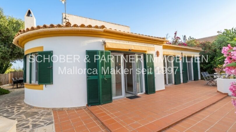 Außenansicht Chalet Cala Murada: weiße Fassade, grüne Fensterläden, Terrakotta-Terrasse, mediterraner Garten.