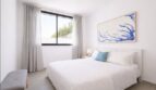 Helles Schlafzimmer mit Doppelbett, blauem Akzent-Kissen, großem Wandbild und Fenster mit Gardinenin Palma de Mallorca