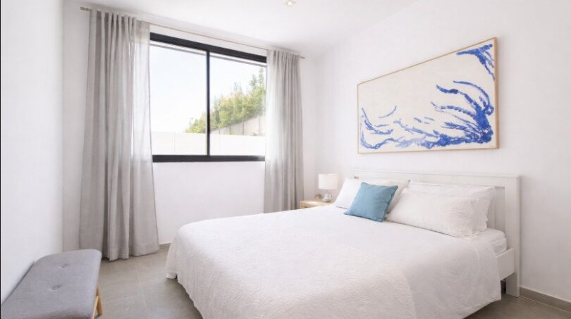 Helles Schlafzimmer mit Doppelbett, blauem Akzent-Kissen, großem Wandbild und Fenster mit Gardinenin Palma de Mallorca
