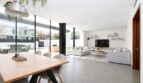 Offener Wohn-Essbereich mit Holztisch, grauer Couch, TV-Wand und Glasfront zum Pool, Einfamilienhaus Palma