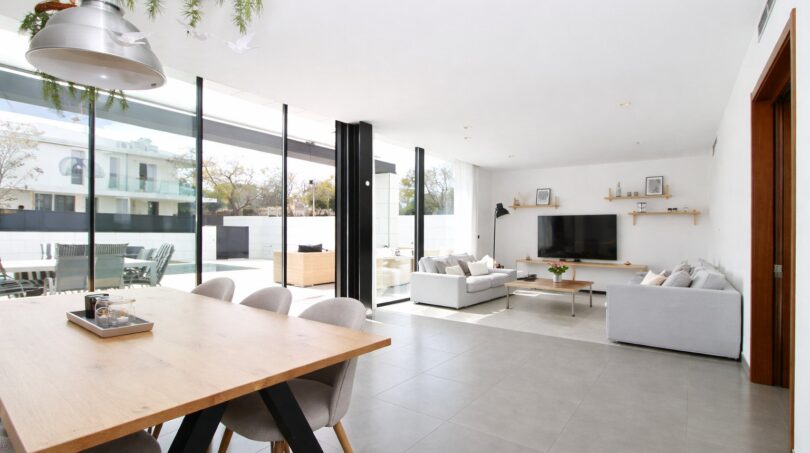 Offener Wohn-Essbereich mit Holztisch, grauer Couch, TV-Wand und Glasfront zum Pool, Einfamilienhaus Palma
