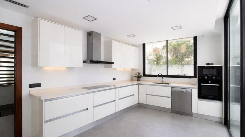 Moderne weiße Einbauküche mit Kochinsel, Induktionsherd und Edelstahlgeräten im Einfamilienhaus Palma de Mallorca