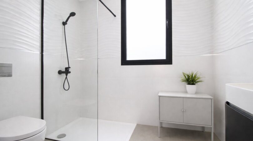 Modernes weißes Badezimmer mit bodenebener Dusche, schwarzen Armaturen und eleganten Wellenstruktur-Fliesen.