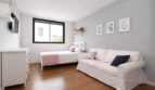 Helles Schlafzimmer mit weißem Sofa, Einzelbett, Holzboden und großem Fenster im Einfamilienhaus Palma
