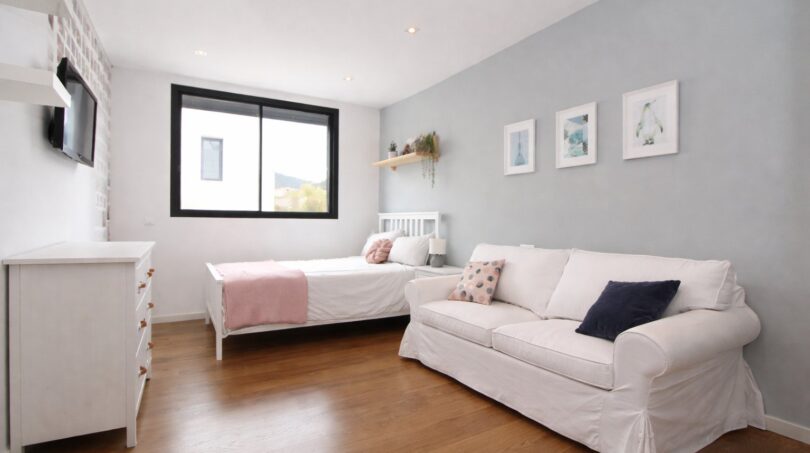 Helles Schlafzimmer mit weißem Sofa, Einzelbett, Holzboden und großem Fenster im Einfamilienhaus Palma