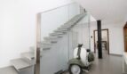 Modernes Eingangsfoyer mit freitragendem Treppenhaus, Glasgeländer und vintage Vespa-Roller als Designelement.