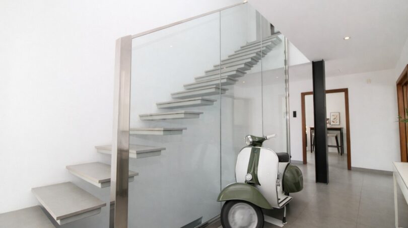 Modernes Eingangsfoyer mit freitragendem Treppenhaus, Glasgeländer und vintage Vespa-Roller als Designelement.