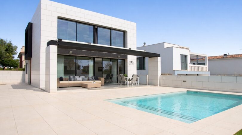 Moderne Villa in Palma de Mallorca mit Pool, Terrasse und großen Glasfronten unter blauem Himmel.