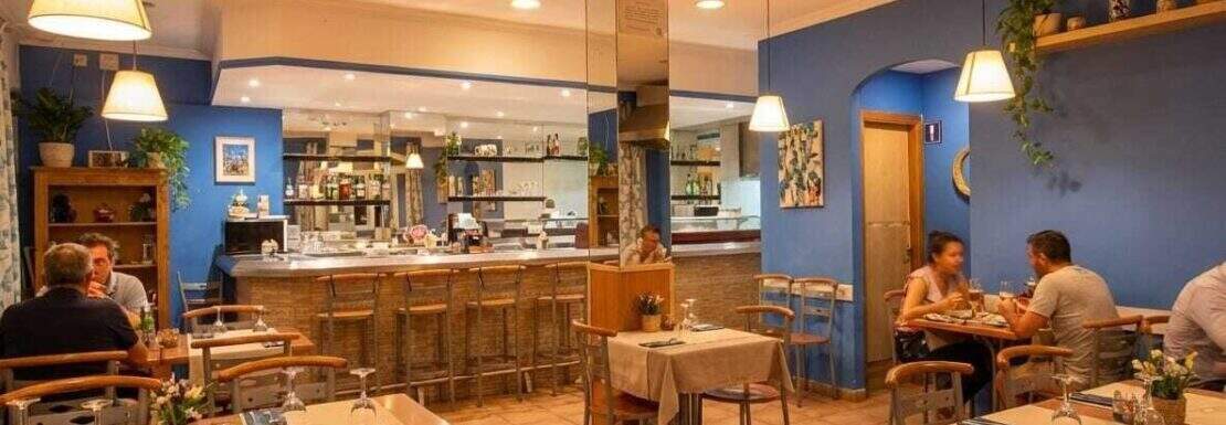 Restaurant mit blauer Wandgestaltung, Holzmöbeln, Bartheke und warmer Beleuchtung in Palma de Mallorca.