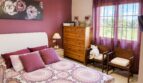 Gemütliches Schlafzimmer mit Doppelbett, lila Akzentwand, Holzkommode und Fenster mit Landschaftsblick in Sencelles.