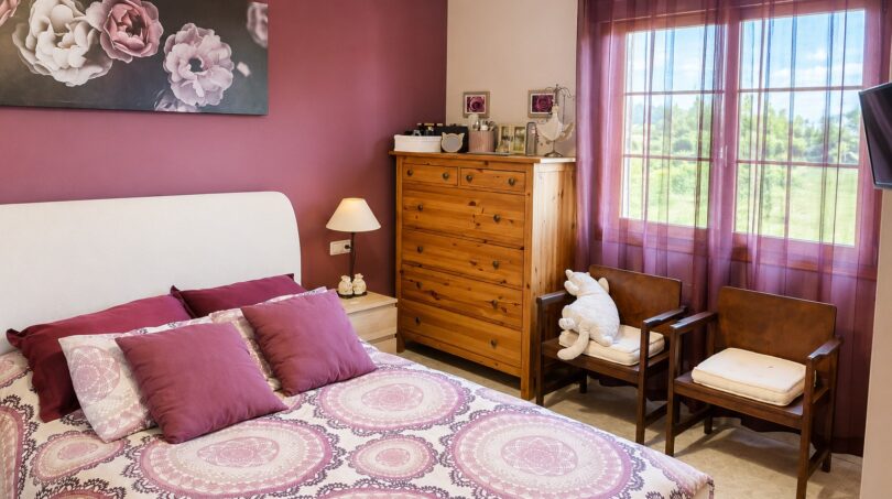 Gemütliches Schlafzimmer mit Doppelbett, lila Akzentwand, Holzkommode und Fenster mit Landschaftsblick in Sencelles.