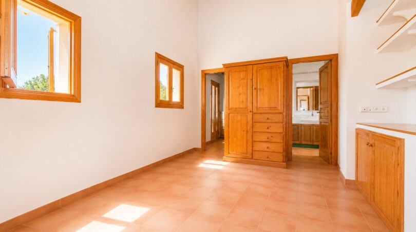 Helles Schlafzimmer der Finca in Marratxí mit Holzbalkendecke, Terrakottaboden und eingebautem Kiefernholzschrank.
