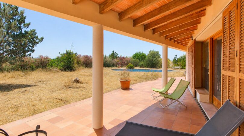 Überdachte Terrasse der Finca in Marratxí mit Holzbalken, Terrakottaboden, Loungestühlen und Blick auf Pool und Garten.