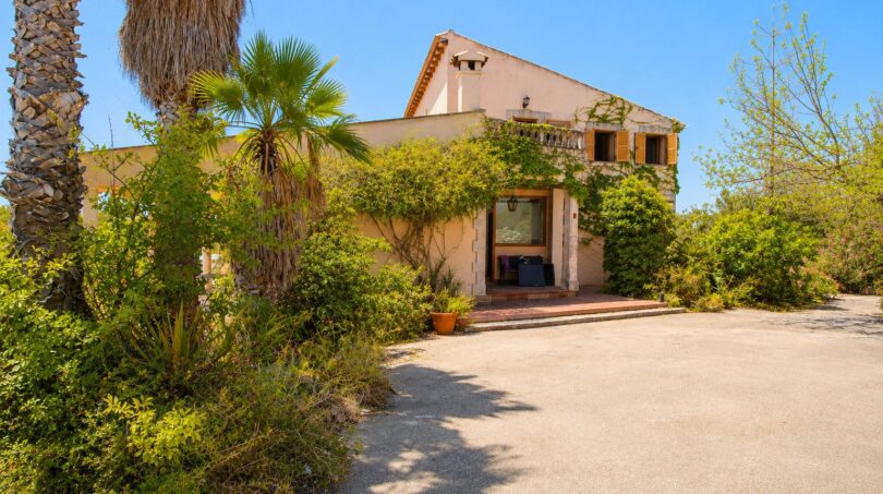 Außenansicht der Finca in Marratxí mit üppiger Begrünung, Palmen und mediterraner Steinfassade.