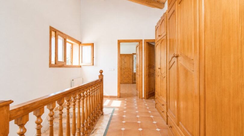 Heller Flur der Finca Marratxí mit Holzbalken, Terrakottaboden, Holzgeländer und eingebauten Holzschränken