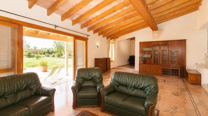 Helles Wohnzimmer der Finca in Marratxí mit Holzbalkendecke, grünen Ledersofas und Blick in den Garten.