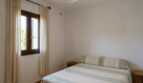 Dormitorio luminoso de la finca en Lloseta con cama doble, ventilador de techo y ventana con cortina.