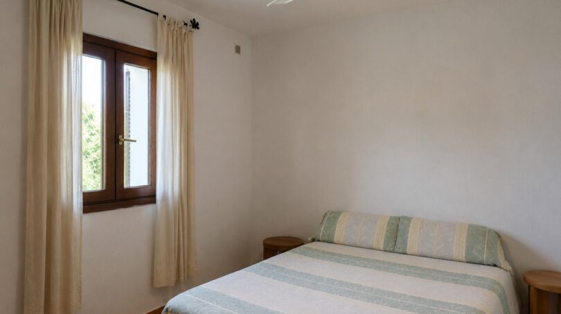 Dormitorio luminoso de la finca en Lloseta con cama doble, ventilador de techo y ventana con cortina.
